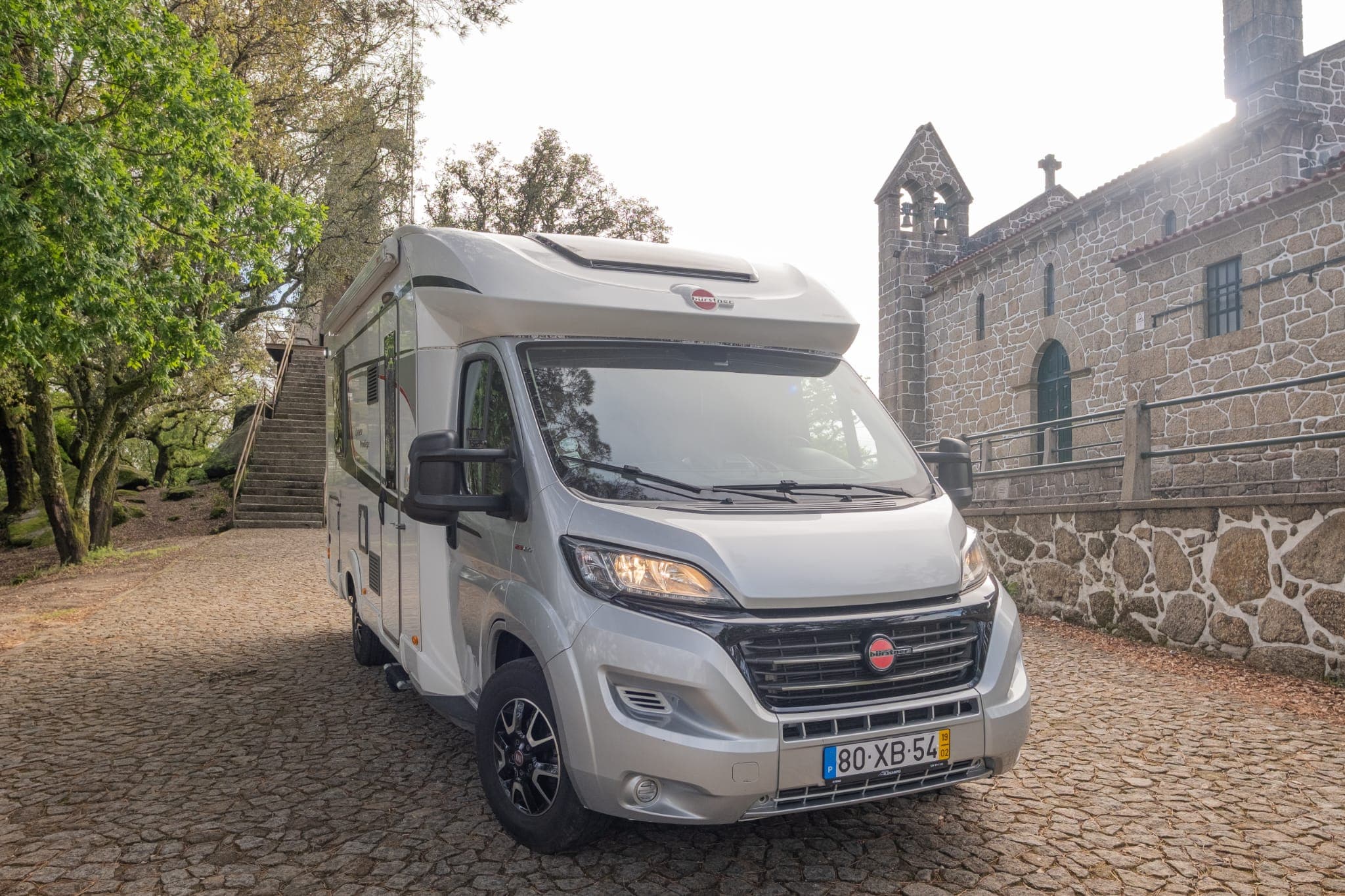 Autocaravana de frente, estacionada num largo de pedra junto a uma igreja