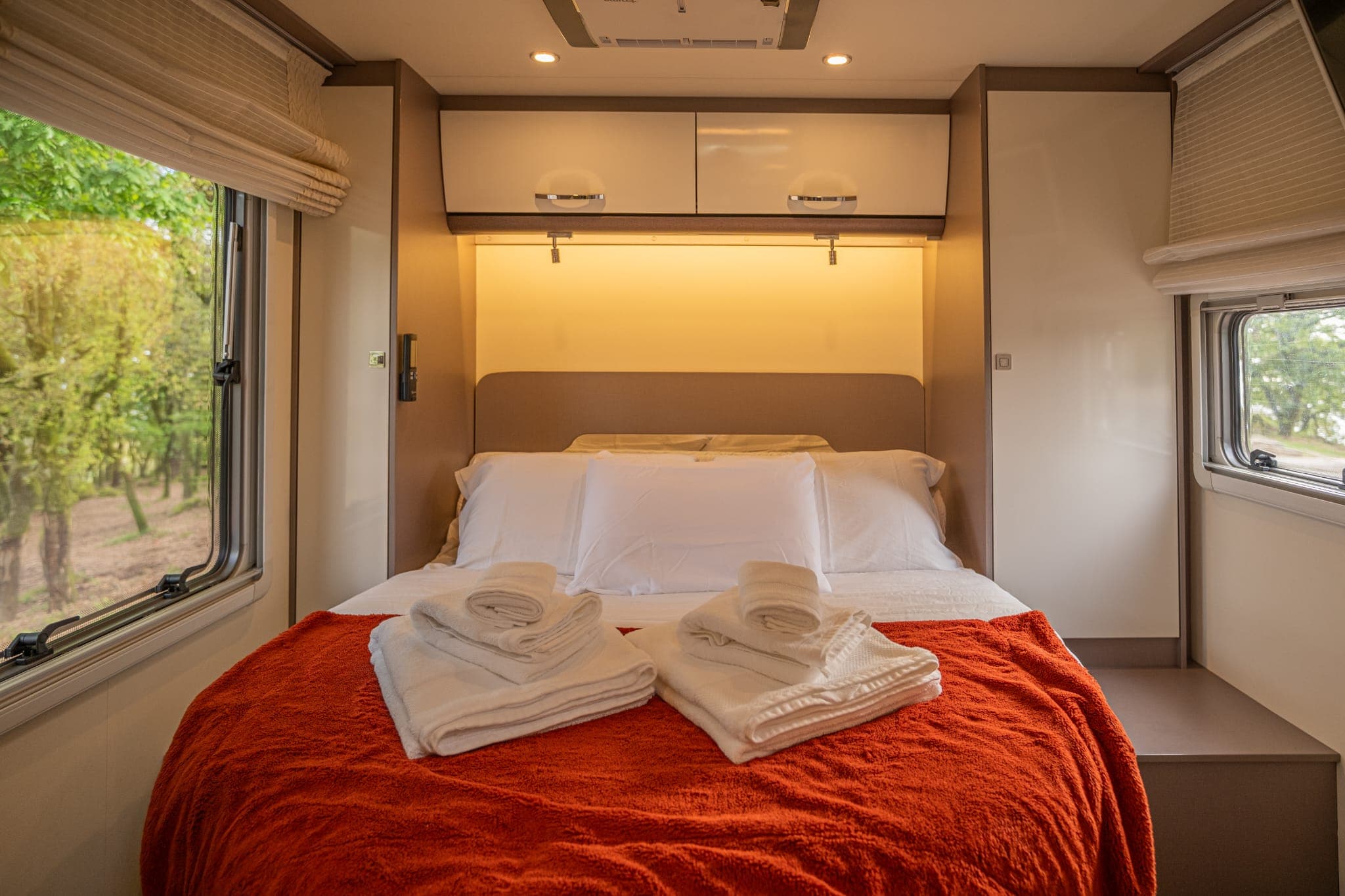 Cama de casal com toalhas dobradas e manta laranja